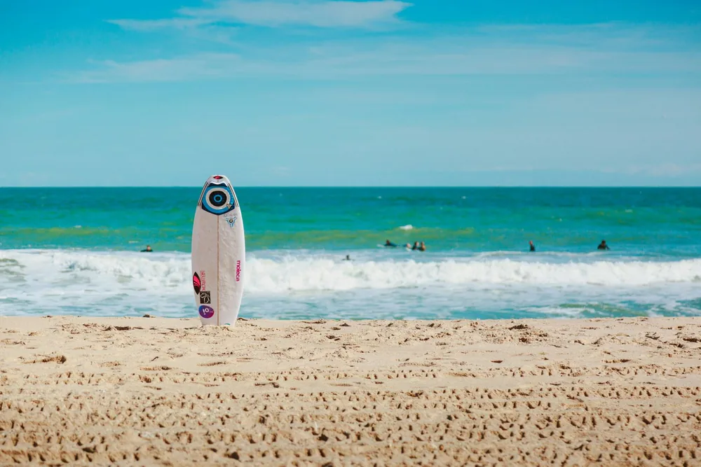A surfboard standing on the beach in front of the ocean